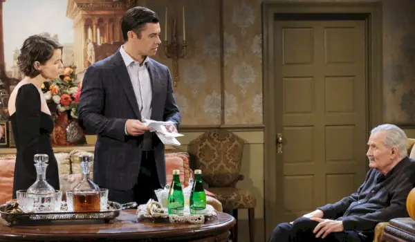 Xander stojí se Sarah, drží bankovky a zírá na sedícího Victora v sídle Kiriakis
