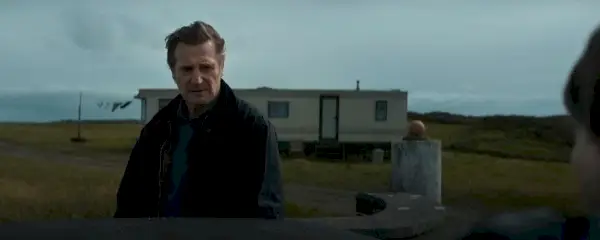 Liam Neeson filme šventųjų ir nusidėjėlių šalyje, jo personažas stovi priešais karavaną ir atrodo susirūpinęs