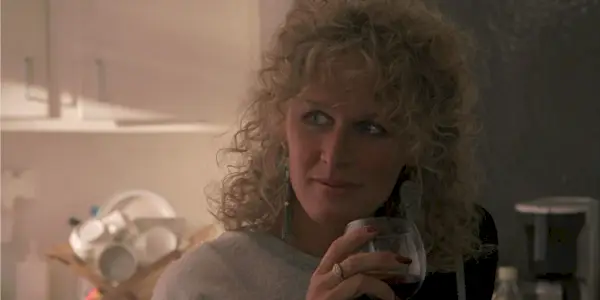 Glenn Close nei panni di Alex in Attrazione fatale con in mano un bicchiere di vino e guardando a sinistra