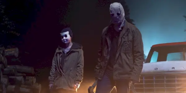 Zamaskowani zabójcy stojący przy ciężarówce w pierwszym rozdziale The Strangers