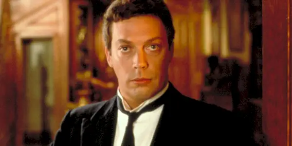 Tim Curry ako Wadsworth, stojaci vo dverách a intenzívne vyzerajúci v Clue