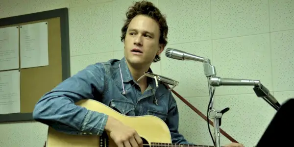 Heath Ledger gra na gitarze i siedzi za mikrofonem.