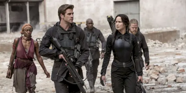 Liam Hemsworth e Jennifer Lawrence como Gale e Katniss caminhando com rebeldes em Jogos Vorazes: A Esperança Parte 1.