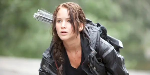 Katniss agachada e olhando para longe em Jogos Vorazes.