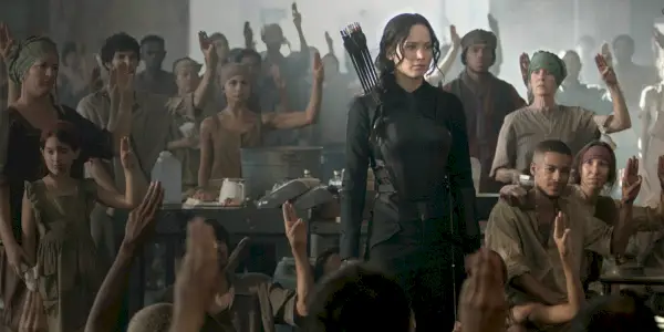 Katniss no Hospital do Distrito 8 dos Jogos Vorazes cercada por pessoas fazendo a saudação de três dedos.