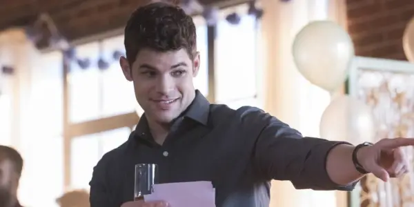 Jeremy Jordan wskazuje na kogoś poza kamerą podczas toastu w Supergirl