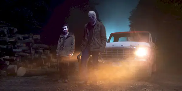 L'homme au masque et la pin-up debout devant un camion la nuit dans The Strangers Chapitre 1