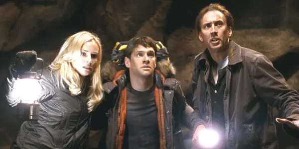 Ben, Abigail e Riley alzano lo sguardo mentre accendono le torce in una grotta nel National Treasure Book of Secrets
