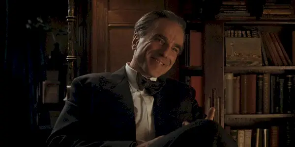 Reynolds Woodcock sitter i en stol og smiler i Phantom Thread.