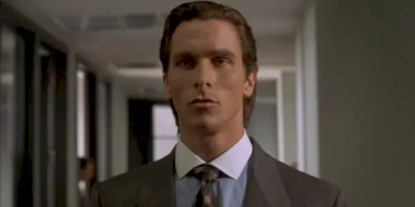 Patrick Bateman (Christian Bale) cammina lungo i corridoi del suo ufficio perso nei suoi pensieri in American Psycho.