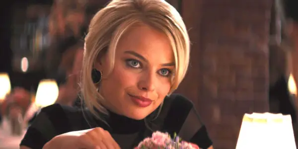 Margot Robbie ako Naomi vo filme Vlk z Wall Street na večeri v luxusnej reštaurácii so šibalským výrazom na tvári