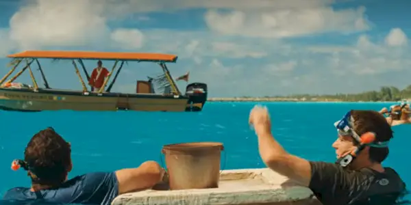 Dois amigos flutuam na água com máscaras de mergulho e um barco ao fundo.