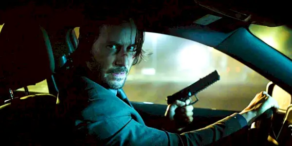 Keanu Reeves conduisant une voiture avec une arme à la main dans John Wick 4