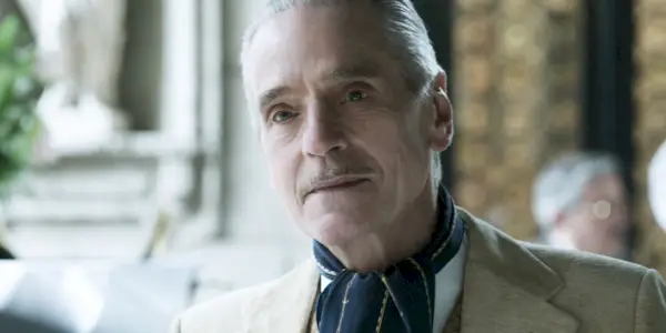 Jeremy Irons sentado y mirando a través de una mesa en House of Gucci