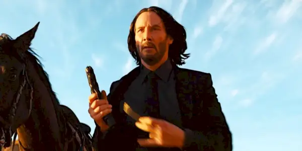 John Wick (Keanu Reeves) recarregando uma pistola ao lado de um cavalo em John Wick: Capítulo 4