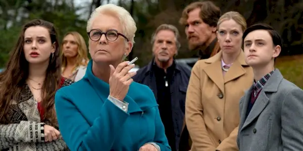 Jamie Lee Curtis fumando um cigarro com a família atrás dela em Knives Out.