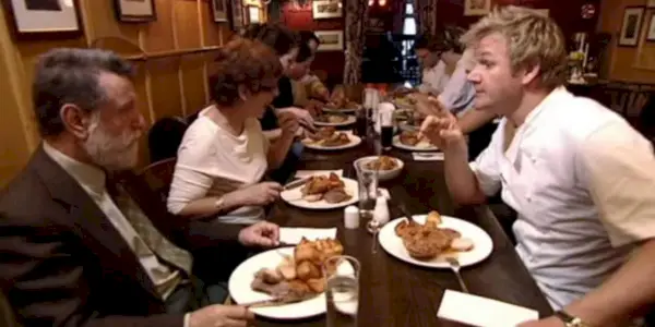 Gordon Ramsay assis à une table avec des convives dans une scène d'un épisode de Kitchen Nightmares