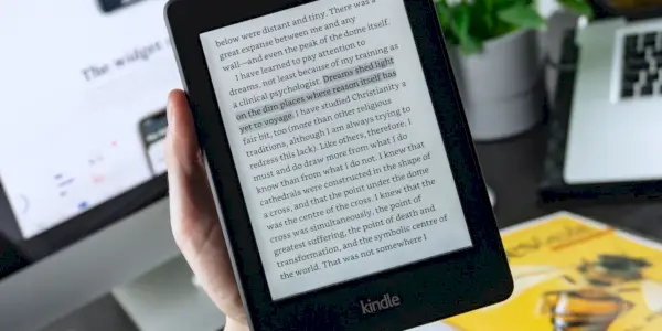 Fotografia osoby, ktorá drží Kindle pred stolom