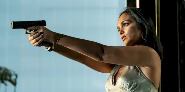 Shalini Peiris punta una pistola fuori campo mentre indossa un vestito argentato