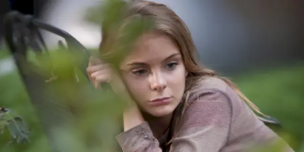 Lizzie Samuels z Walking Dead sa opiera o zbraň a vyzerá smutne.