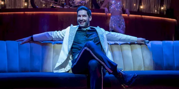 Tom Ellis als Luzifer saß auf einer Couch und grinste in Lucifer Staffel 6, Folge 6