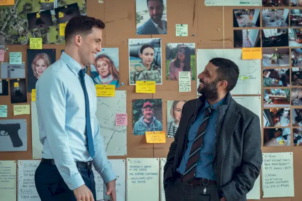 dino fetscher som politibetjent marty mcgreggor, adeel akhtar som ds sami kierce smiler til hinanden foran en politibevis-opslagstavle på netflix