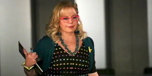 Kirsten Vangsness como Penelope Garcia sorrindo e segurando uma prancheta em Criminal Minds