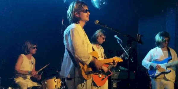 Joe Keery spielt Gitarre auf der Bühne in einem weißen Anzug