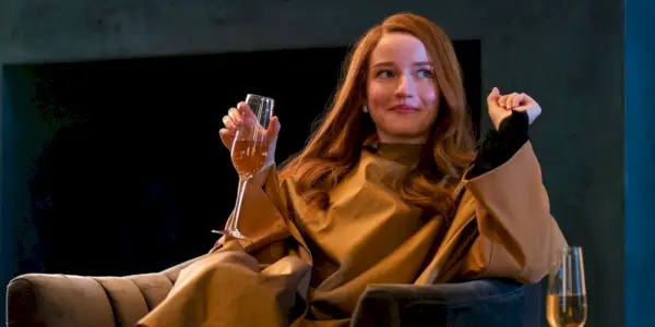 Julia Garner sentada en una silla con una copa de vino en Inventing Anna