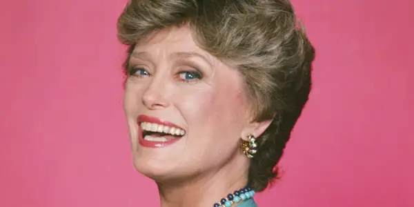 The Golden Girls의 블랑쉬 역을 맡아 분홍색 배경 앞에서 웃고 있는 Rue McClanahan