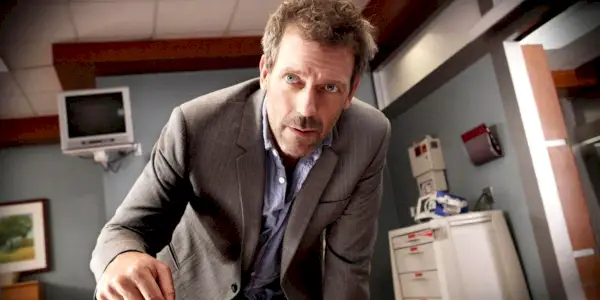 Hugh Laurie jako House pochylający się nad stołem w House M.D.