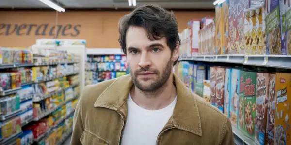 Tom Bateman står i en korngang med et alvorligt udtryk i ansigtet.