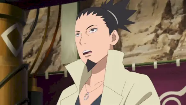 Skjermbilde fra Boruto-anime viser Shikamaru gjør seg klar til å snakke med en gruppe studenter mens han står foran et Konoha-banner.