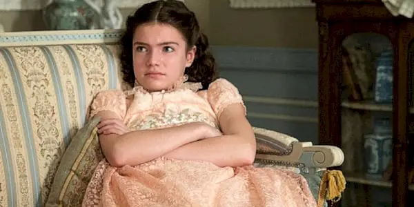 Hyacinth assise sur un canapé, les bras croisés dans Bridgerton