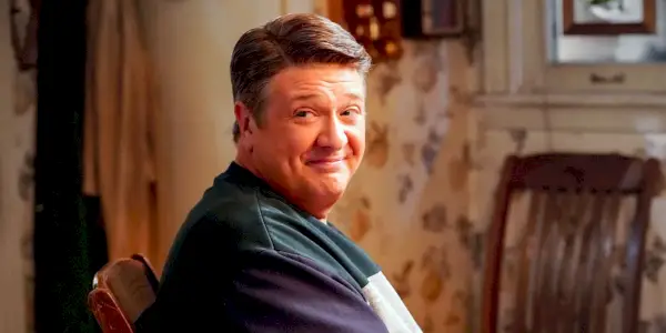 George Sr. sedí u stolu a usmívá se v Young Sheldon