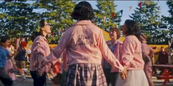 Ružové dámy držiace sa za ruky v kruhu v Grease: Rise of the Pink Ladies