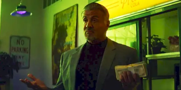 Sylvester Stallone in Tulsa King tiene in mano una pila di soldi con un'espressione compiaciuta sul viso.