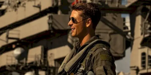 El ahorcado con gafas de sol y sonriendo mientras está de pie en la cubierta de un barco en Top Gun Maverick