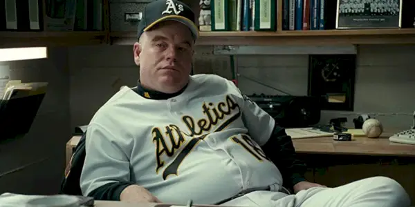 Phillip Seymour Hoffman siedzi przy biurku w koszulce baseballowej w Moneyball