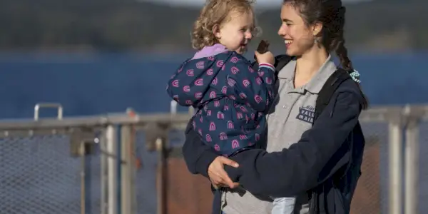 Alex hält Maddy und lächelt in Maid am Wasser