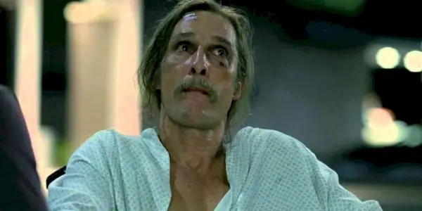 Matthew McConaughey ako Rust Cohle s dlhými vlasmi a fúzmi v nemocničnom plášti v 1. sezóne True Detective