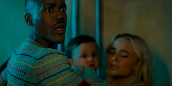 Doktor (Ncuti Gatwa) s prekvapeným výrazom sa snaží ochrániť Ruby (Millie Gibson), ktorá nesie malého Erica na rukách v seriáli Doctor Who 14, ep 1